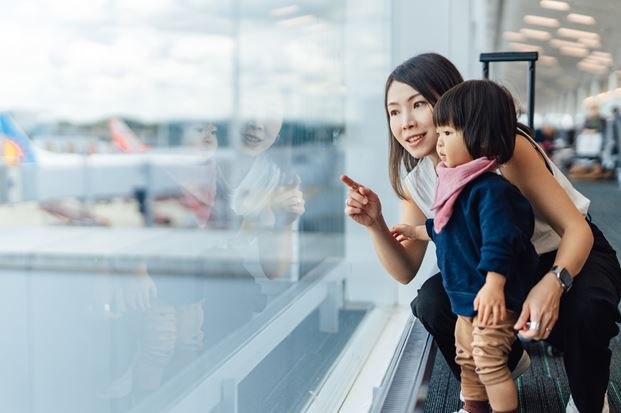 Brown haired lady and her child looking through a window at planes on the runway 